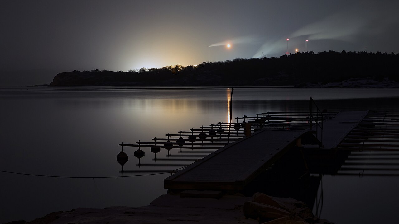 Refinería de Preemraff iluminada al otro lado de Brofjorden, Suecia, de noche.